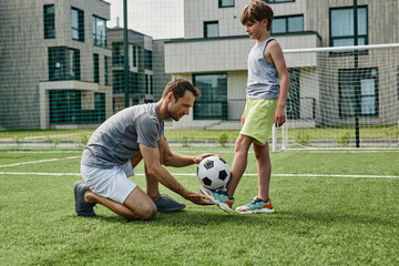 Side view portrait of young father teaching son football in outdoor court, copy space