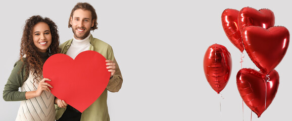 Young couple in love and heart-shaped balloons on light background. Banner for Valentine's Day...