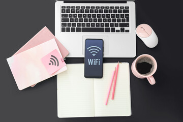 Stationery supplies, laptop, computer mouse, cup of coffee and mobile phone with WiFi symbol on dark background