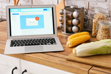 Vegetables and modern laptop with opened e-mail box on wooden counter in kitchen