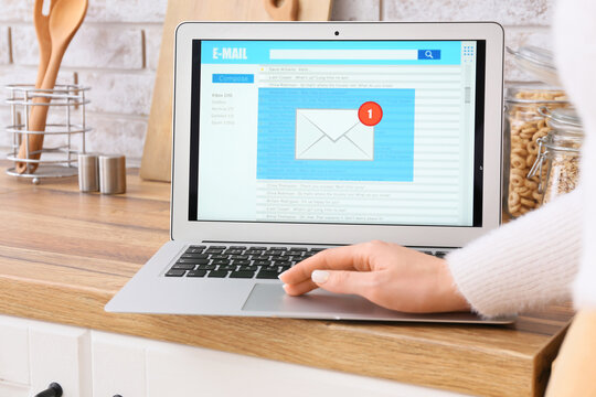 Woman using laptop with opened e-mail box on wooden counter in kitchen