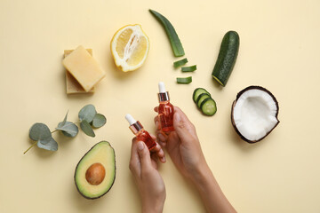Female hands with bottles of essential oil and ingredients on color background