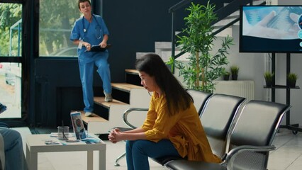 Female nurse taking patient to attend consultation with specialist, sitting in waiting room at facility. Asian woman waiting to talk to doctor about healthcare medicine at checkup visit.