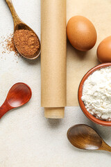 Roll of baking paper, bowl with flour and wooden spoon on light background, closeup
