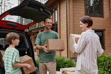 Portrait of happy family unloading boxes from car trunk while moving into new house in nature © Seventyfour