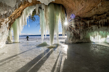 The rising sun shines into an ice cave on Lake Superior. A man trekking across the ice shows the scale of how large it is