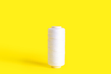 Fototapeta na wymiar White thread spool on yellow background