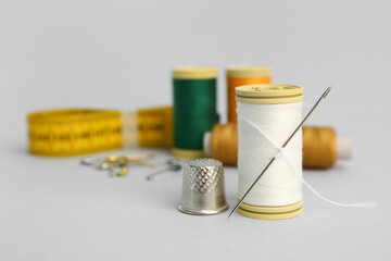 Thread spool with needle and thimble on grey background