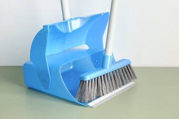 Blue dustpan and broom on floor near light wall, closeup