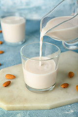 Pouring almond milk from gravy boat into glass on color background, closeup