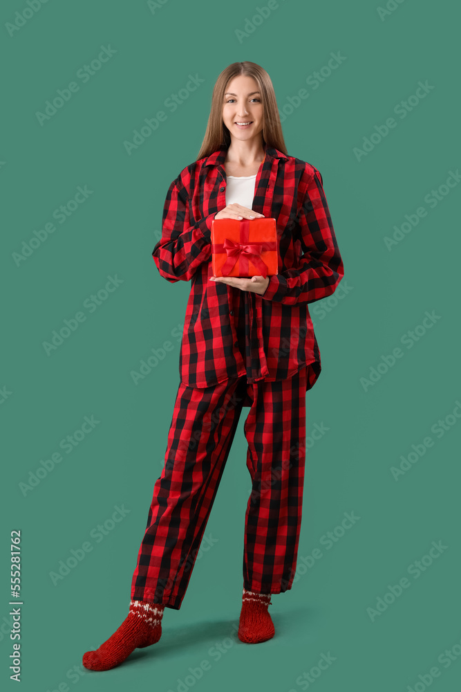 Sticker Young woman in checkered pajamas with Christmas gift on green background