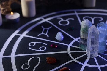 Natural stones for zodiac signs, drawn astrology chart and burning candle on black table, closeup