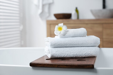 Stacked bath towels and beautiful flower on tub tray in bathroom. Space for text