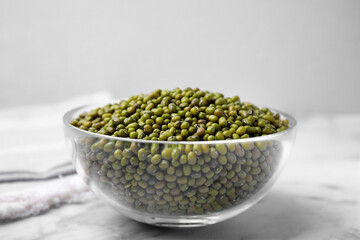 Glass bowl with green mung beans on white marble table, closeup