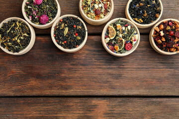 Different kinds of dry herbal tea in bowls on wooden table, flat lay. Space for text