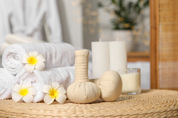Fototapeta na wymiar Herbal bags, candles, rolled towels and beautiful flowers on wicker surface indoors. Spa products