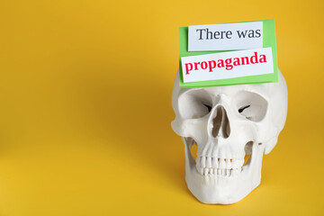 Information warfare concept. Human skull and paper cards with phrase There Was Propaganda on yellow background, space for text
