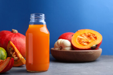 Tasty pumpkin juice in glass bottle and different pumpkins on light grey table against blue background. Space for text