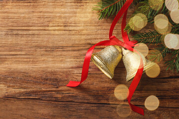 Christmas bells and fir tree branches on wooden table, flat lay. Space for text