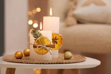 Beautiful burning candles decorated with dry orange slices and cinnamon sticks on white table indoors. Christmas atmosphere