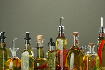Cooking oil with different spices and herbs in bottles on grey background