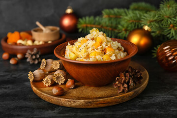 Fototapeta na wymiar Board with bowl of rice Kutya, nuts, fir cones and poppy pods on dark table, closeup