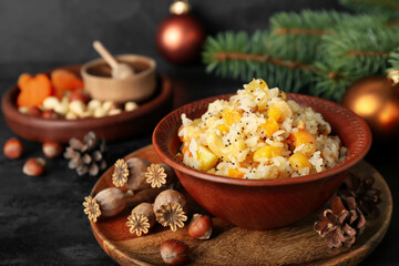 Board with bowl of rice Kutya, nuts, fir cones and poppy pods on dark table, closeup