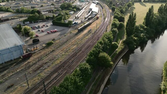 Panning Aerial Drone Shot Looking Down York Railway Line next to the National Railway Museum with Diesel Trains Parked at Sunset with Trees and Parked Cars