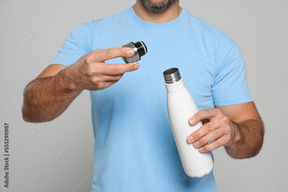 Sticker Man opening thermo bottle on light grey background, closeup