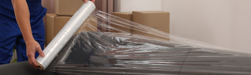Worker wrapping sofa in stretch film indoors, closeup. Banner design