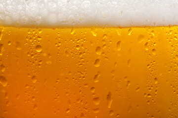 Glass of tasty cold beer with foam and condensation drops as background, closeup