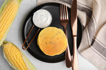 Tasty corn pancakes with sauce served on white tiled table, flat lay