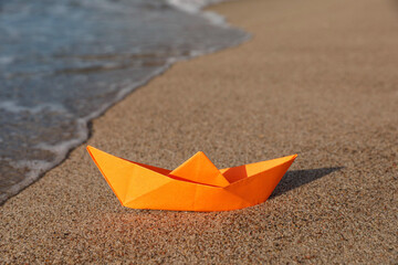 Orange paper boat on sand near sea, space for text
