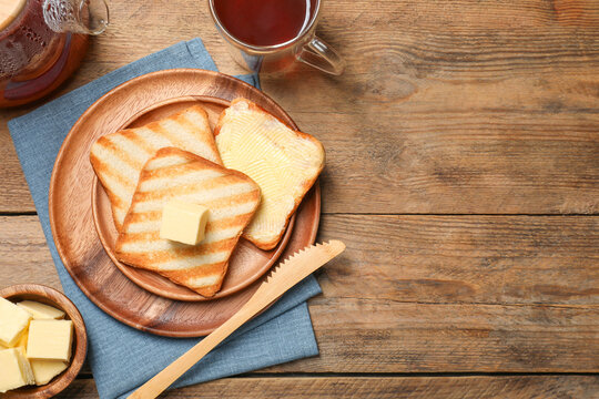 Tasty toasts with butter served on wooden table, flat lay. Space for text