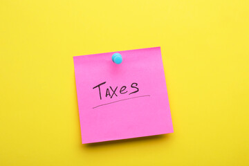 Paper note with word Taxes pinned on yellow background