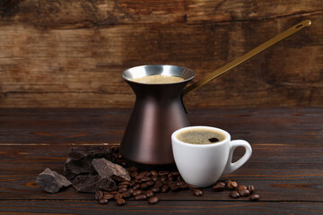 Hot turkish coffee pot, cup of drink, beans and chocolate on wooden table