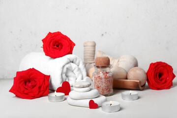 Fototapeta na wymiar Beautiful spa composition for Valentine's Day with stones, candles, sea salt, towel and rose flowers on light background