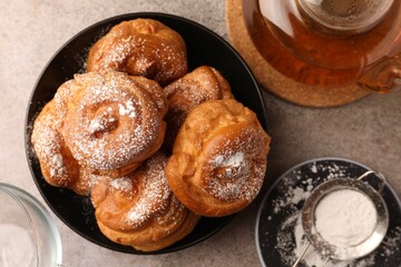 Delicious profiteroles with powdered sugar and tea on grey table, flat lay