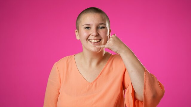 Portrait Of Smiling Happy Gender Fluid Non Binary Young Woman 20s Smiling And Giving CALL ME Gesture With Hands Isolated On Pink Background.