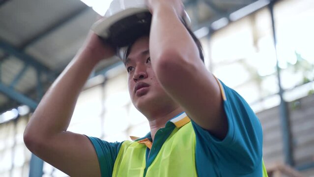 4K, Asian male worker standing in a large factory, He was wearing a reflective vest and was wearing a helmet on his head, To ensure the safety of working in factories that are always at risk.