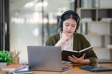 Asian women wearing headphones study online watch webinar podcasts on laptops listen to learning...