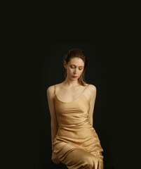 Woman in golden silk satin camisole dress, studio shot.