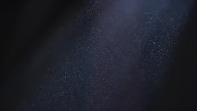 Slow motion close up of dust particles in a beam of sun light against dark background