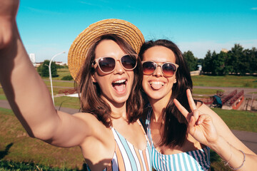 Two young beautiful smiling hipster women posing in the street. Sexy trendy models in summer...