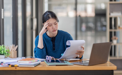 Portrait of tired young business Asian woman work with documents tax laptop computer in office. Sad, unhappy, Worried, Depression, or employee life stress concept.