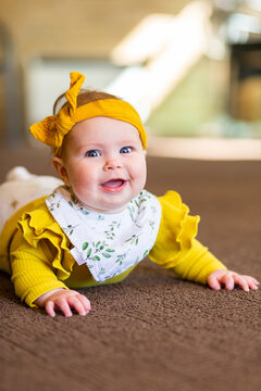 Happy baby dressed up in bright yellow on Sunday lying on carpet