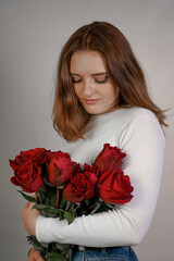 Portrait of a young woman in a white blouse holding a bouquet of roses on a pink background. Valentine's Day