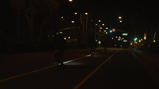 Chase shot following road bikers at night in bike lane in city with traffic lights in background