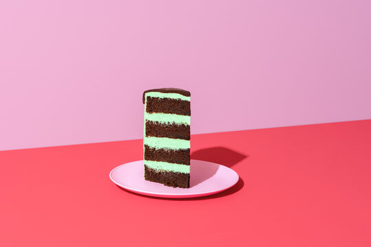 Slice of cake minimalist on a red background. Chocolate and mint layered cake.