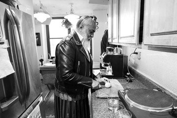 gray haired bearded man in leather jacket cuts a lemon a small kitchen